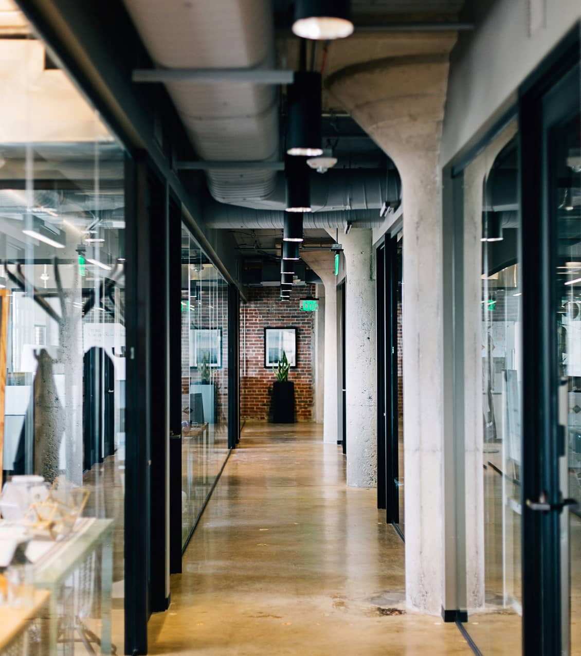 Hallway view with glass walls, wooden floors, and arch-like curved columns