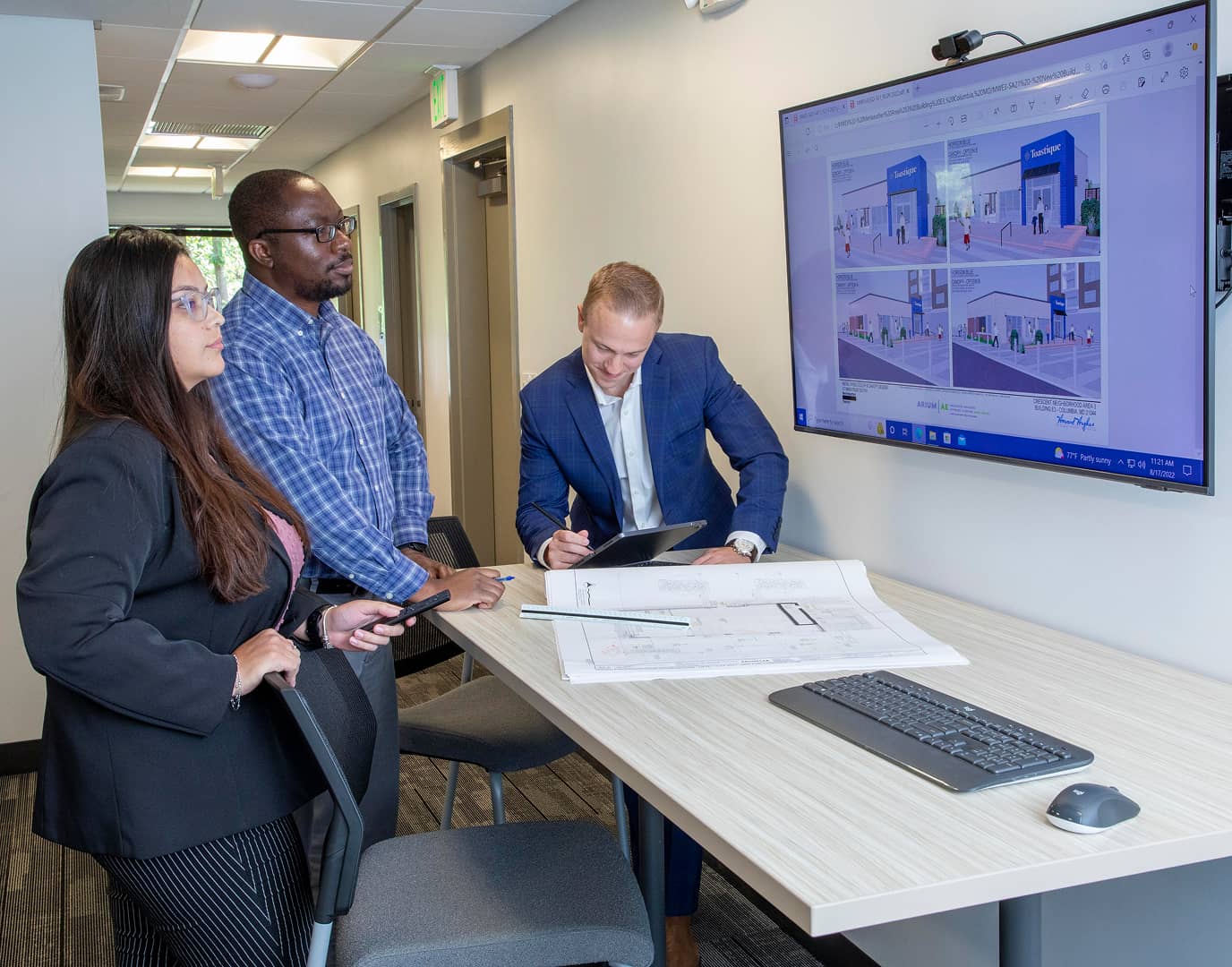 Three people looking at floor plans both on screen and on a large physcal copy